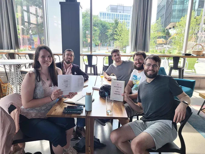 Five people, sitting around a table in front of some large windows, holding copies of the book A Paradise of Small Houses