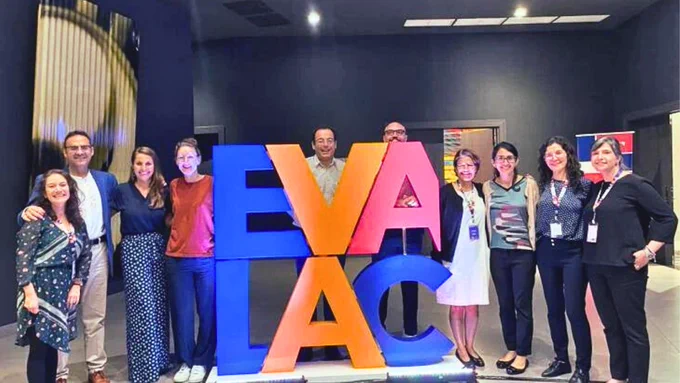 A group of happy, smiling people standing around a sign that says EVALAC. (EVALAC is an initiative by the Office of Evaluation and Oversight of the Inter-American Development Bank to strengthen evaluation capacities in Latin America and the Caribbean.)