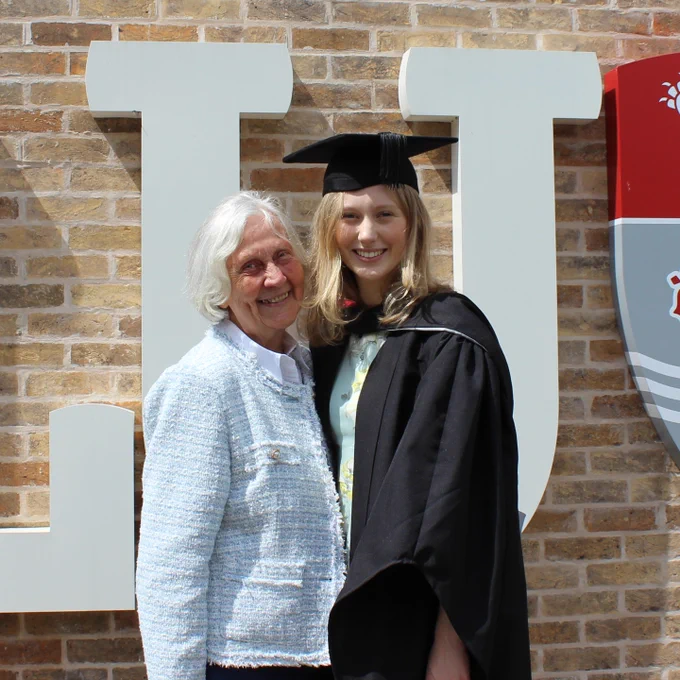 A graduating student poses with a loved one in front of Lancaster logo