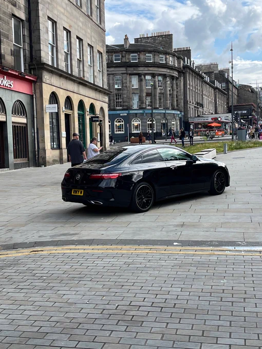 Black Mercedes RIKY M (with illegal anti-APRN plates and incorrect distribution/spacing of letters) parked on pedestrianised area at top of Elm Row, Leith, Edinburgh. Double yellow lines are visible. 