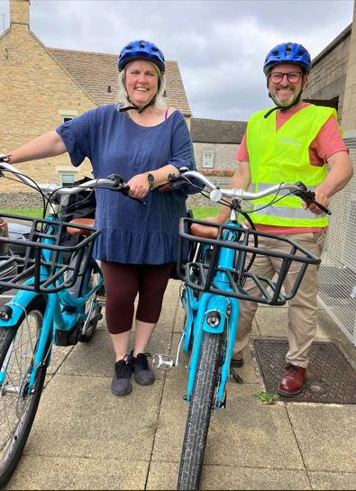 Two beaming people holding blue e-bikes. Photo by Mouse About Town.