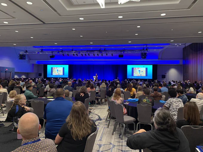 Hotel conference room filled with people listening to the Noyce 2024 opening plenary, delivered by Emily Janssen of StoryCorps.