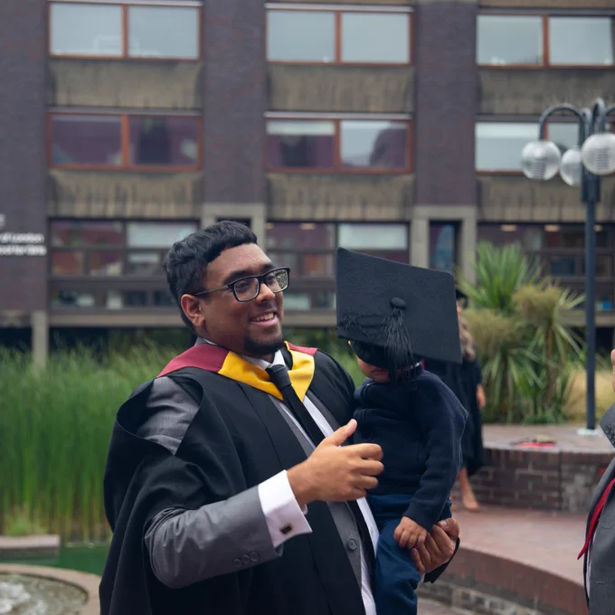 Someone holding a baby whose face is concealed with a graduation cap