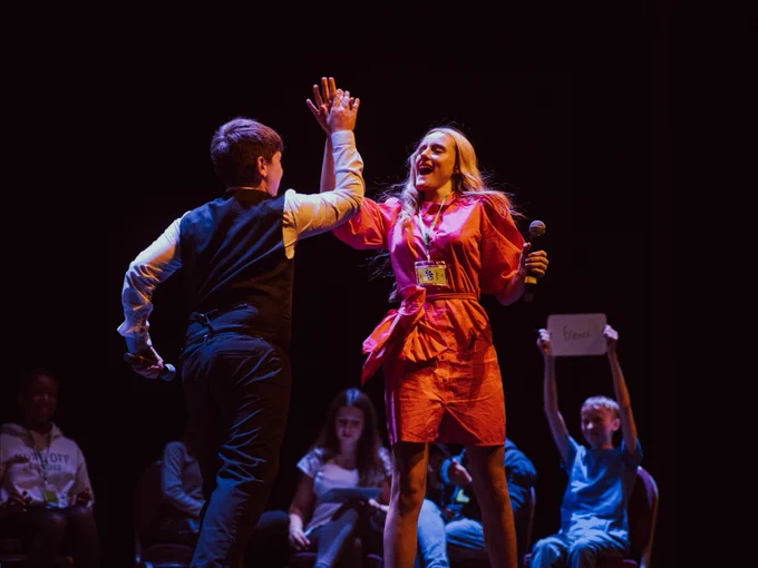 Two participants high-five on stage while other competitors watch in the background under stage lighting.
