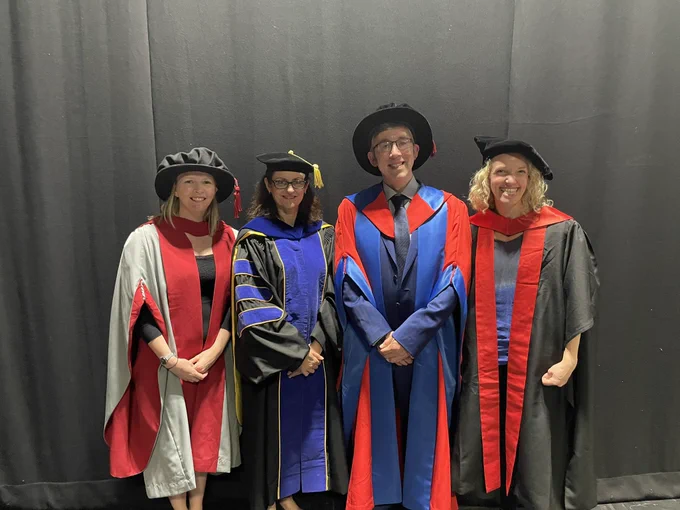 Dr Lucy Balderstone, Dr Sue Broughton, Prof Mick Urbaniak and Dr Lucy Jackson-Jones in gowns against a black backdrop