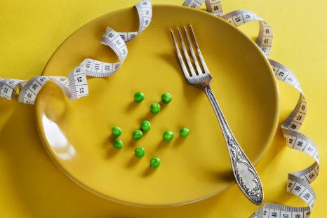 Sur cette photographie se trouve une assiette jaune contenant 11 petits pois et une fourchette. Autour de l'assiette se trouve un mètre ruban.
© Photo de Elena Leya sur Unsplash