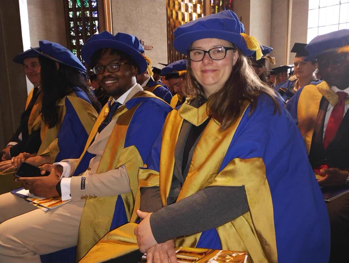 Two postgraduate researchers with gown and hat sat together in ceremony