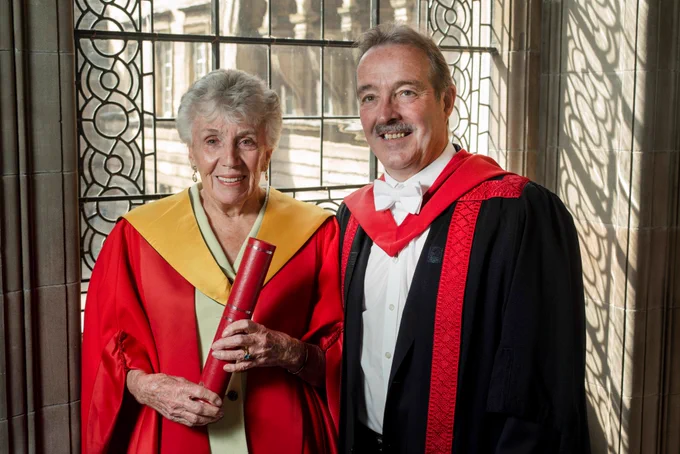Daughter of Eric Liddell, Patricia Liddell Russell pictured with Chair of Sport Grant Jarvie in graduation robes holding degree.