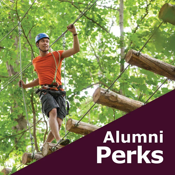 person outdoors wearing safety gear, walking across a bridge using ropes to help them get across.