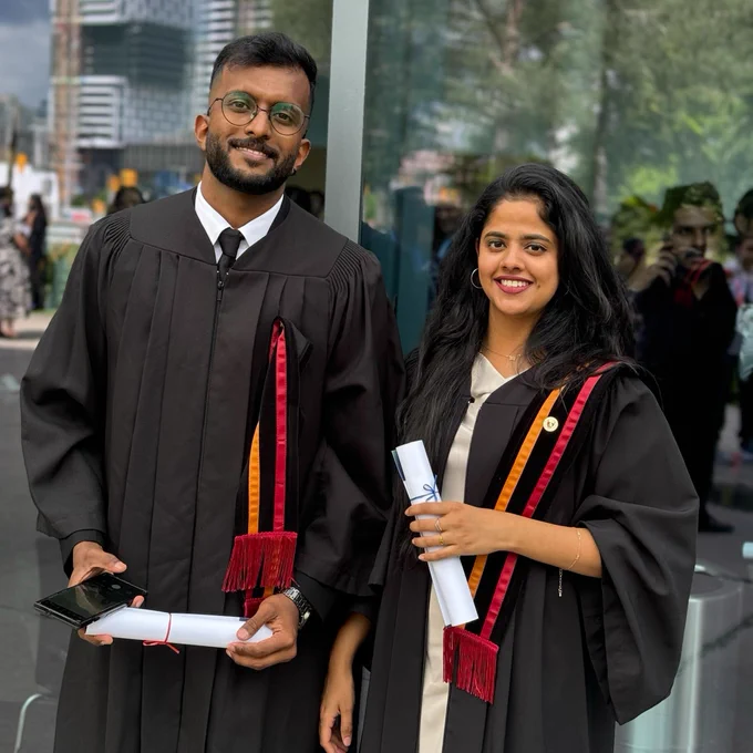 Two graduates wearing their gown and liripipe smiling at the camera.