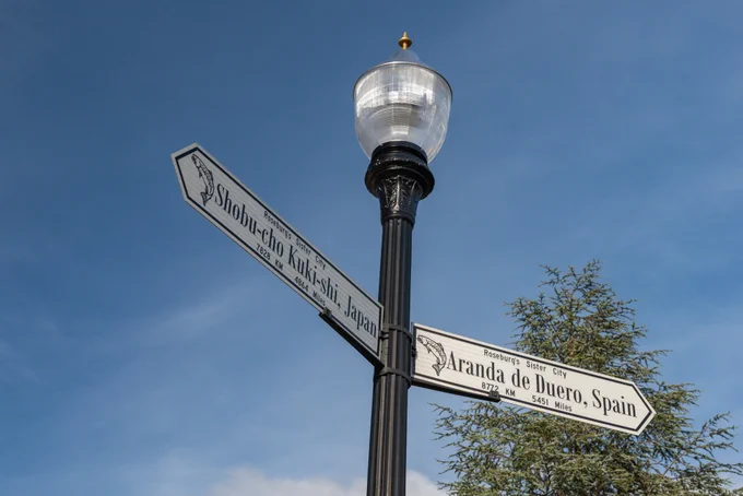 Light post featuring street signs indicating Roseburg's Sister Cities Shobu-cho Kuki-shi, Japan and Aranda De Duero, Spain
