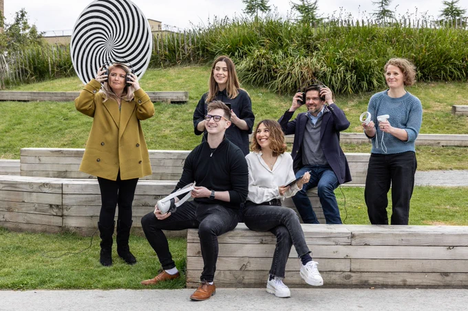 Several people sitting on a bench next to a big black and white sculpture.