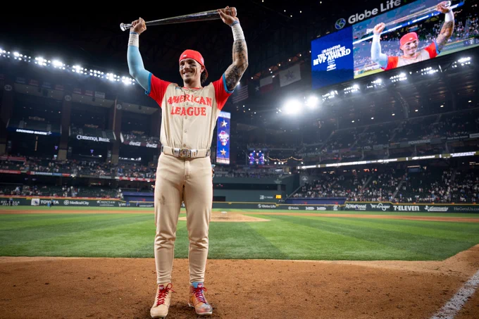 Jarren Duran holds up crystal/glass bat over his head, the All-Star MVP trophy, and smiles at home plate. He wears the American League All-Star uniform at Globe Life Park. 