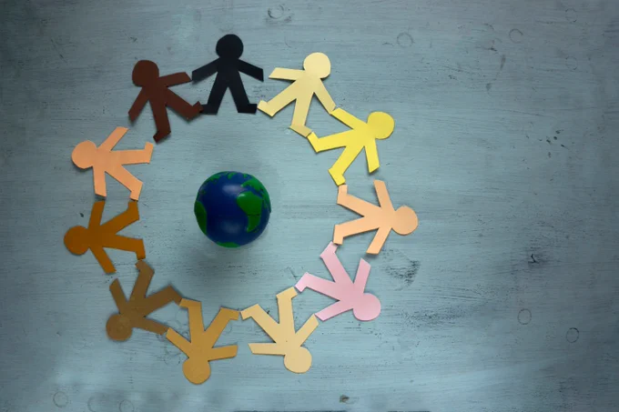 Different coloured paper cutouts of people all holding hands in a circle around the world. 