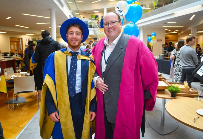 Two people stood together in graduation clothing smiling 