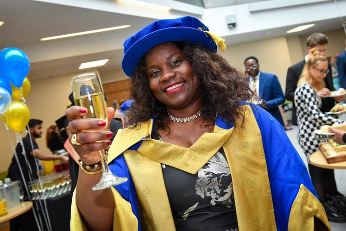 Person at graduation in postgraduate gown and cap smiling and holding cap for photo