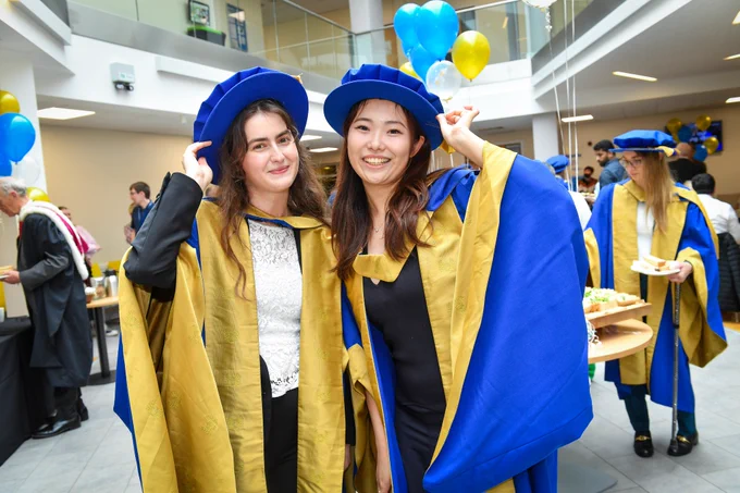 Two people smiling and holding caps celebrating their graduation 