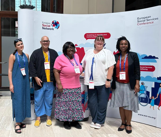 Members of the National Co-production Advisory Group and the Think Local Act Personal team stand in front of a banner at the European Social Services Conference.