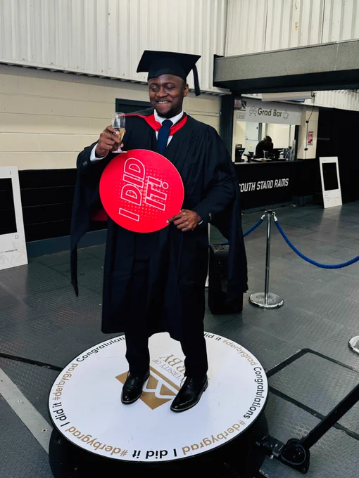 A graduate on a rotating camera platform. The graduate is holding a sign which states "I did it!"
