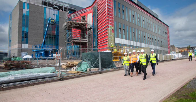 A group of people wearing high visibility vests and hard hats walk past a partially constructed building