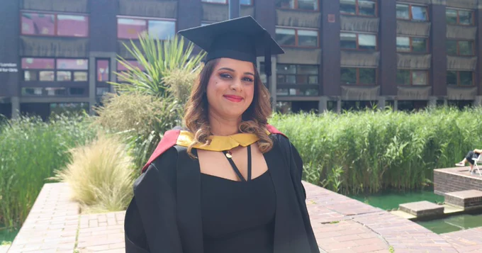 A photo of Riya standing outside in her graduation cap and gown