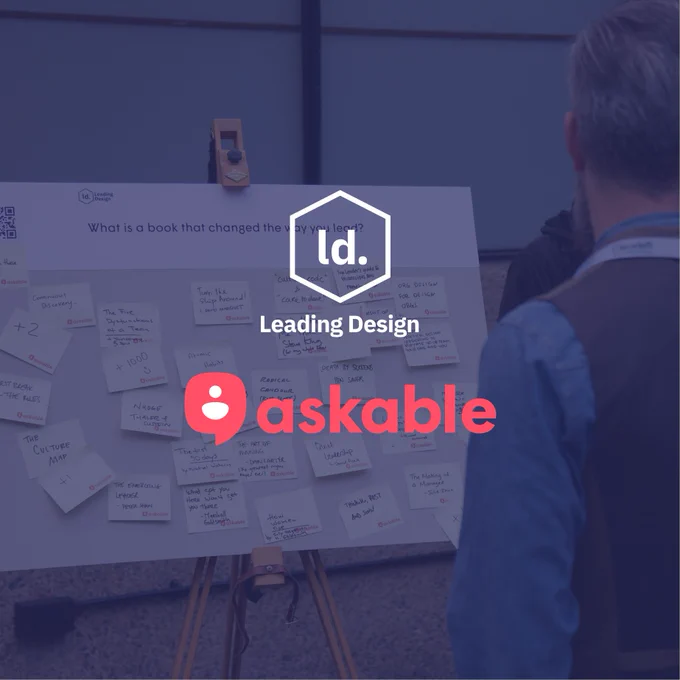 A person stands in front of a whiteboard filled with Post-it notes, which carry handwritten suggestions for "a book that changed the way you lead." The backdrop features two stacked company logos: "Leading Design" and "askable.