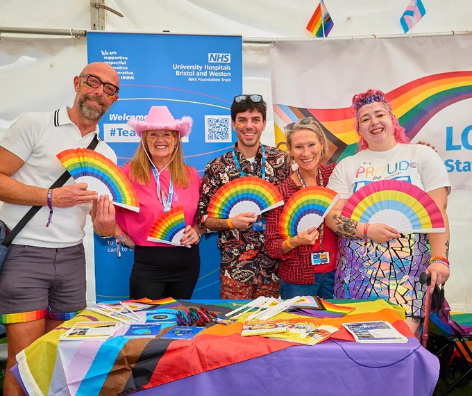 UHBW staff holding rainbow fans at the UHBW stall in the community tent at Bristol Pride. 