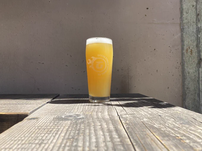 a bright yellow pint of beer sits on a wooden bench in the beer garden on a bright sunny day.