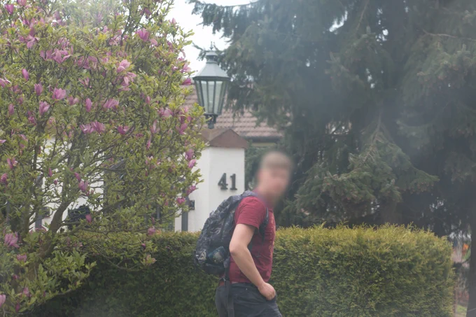 Ein junger Mann in der Mitte des Bildes schaut in die Kamera, sein Gesicht ist unkenntlich gemacht. Im Hintergrund ein Baum, Büsche und die Hausnummer 41 von dem Anwesen von Neonazi Funktionär Thorsten Heise