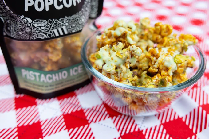 A bag of Pistachio Ice Cream sits on a red checked picnic blanket next to a bowl of its popcorn.