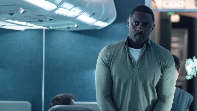 From Hijack. Idris Elba as Sam Nelson stands in the aisle of an airplane with a serious look on his face.