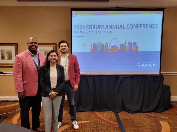 Three speakers in front of presentation screen with the title "2024 FORUM ANNUAL CONFERENCE"