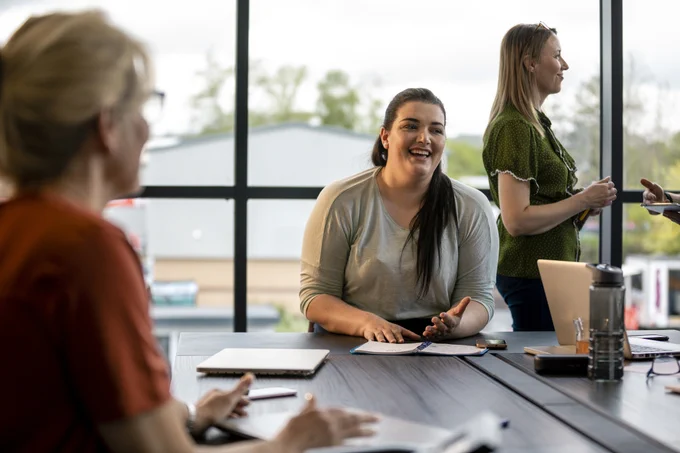 A lady at a desk writing in a notepad smiling.