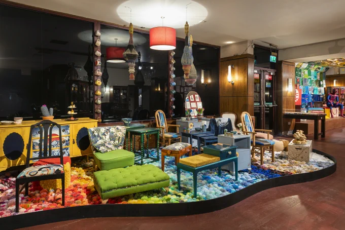 A display of colourful furniture on a bed of colour pom poms organised by colour to form a rainbow