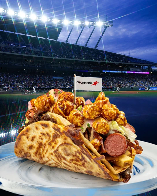 A photo of the Royals "Taste of the K Taco" on a blue and white plate. It's in front of a backdrop of Kauffman Stadium.