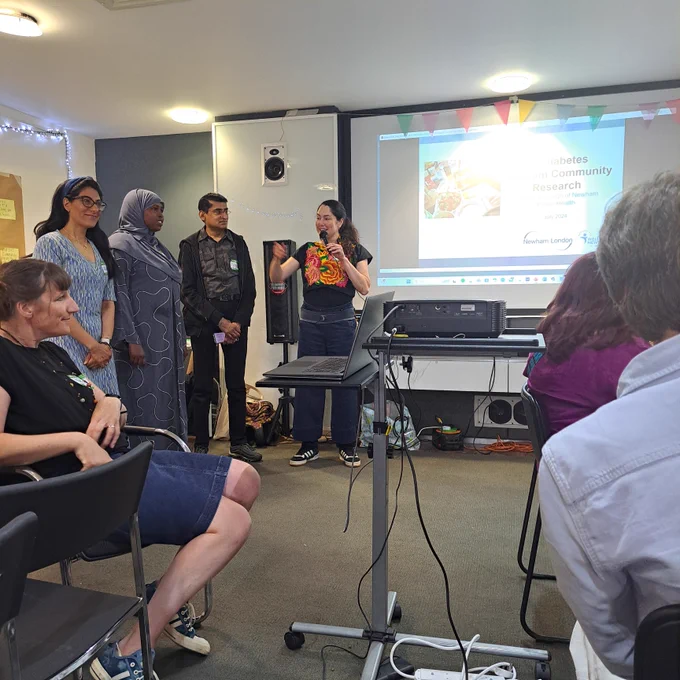 The photo depicts four people standing in front of a projector delivering a presentation.
