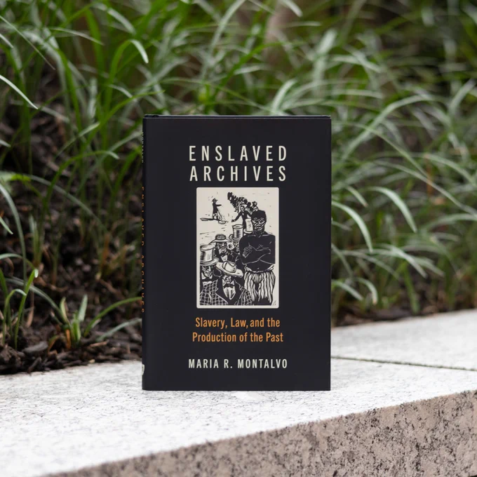 The book "Enslaved Archives: Slavery, Law, and the Production of the Past" by Maria R. Montalvo sitting on a ledge in a garden.