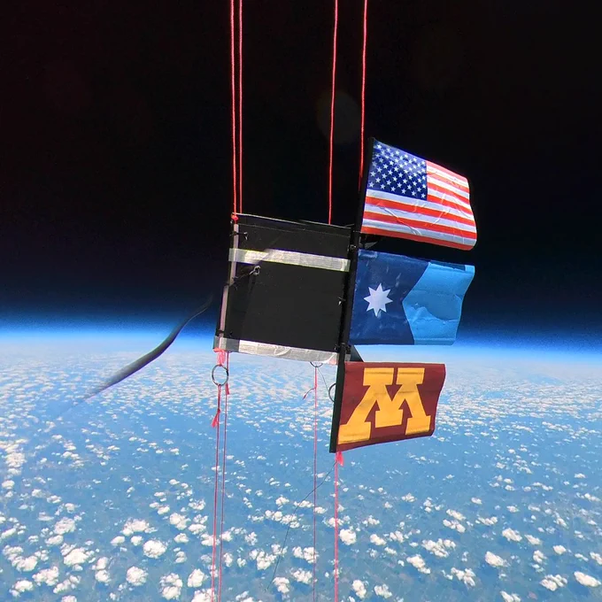 A USA flag, Minnesota State flag, and U of M flag hang from a payload in space