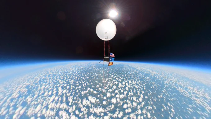 A USA flag, Minnesota State flag, and U of M flag hang from a payload in space showing the curve of the earth