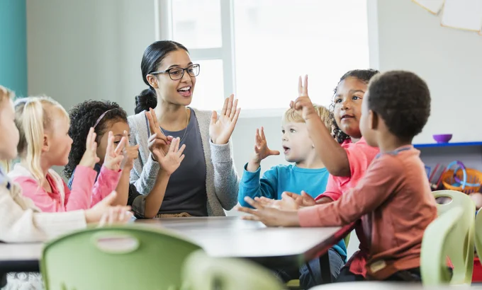 A teacher leading a class of young kids at a table.
