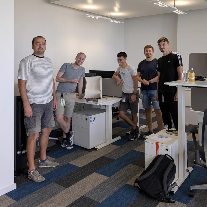 Five software engineers in the Google office Munich around their desks, joyfully looking at the camera and a box of cake.