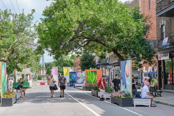 People walk, sit, and converse along a pedestrianized shopping street lined with trees, furniture and art in Montreal.
