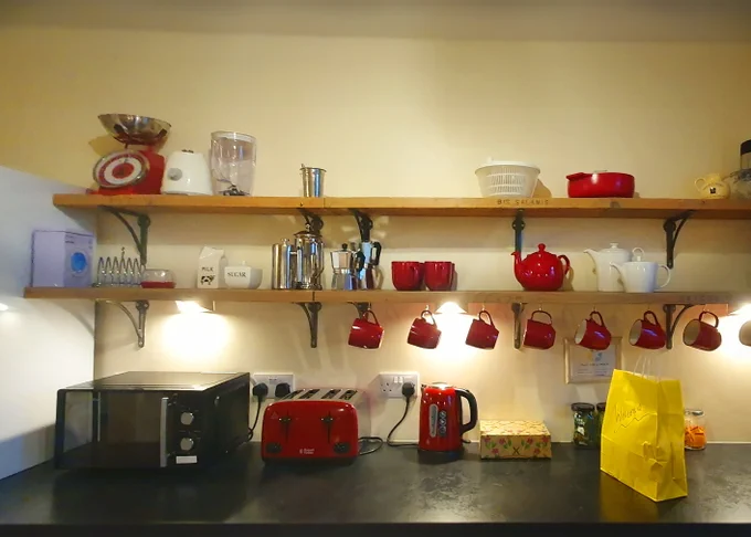 Kitchen shelves above a microwave, toaster and kettle, the shelves have mugs and tea and coffee pots