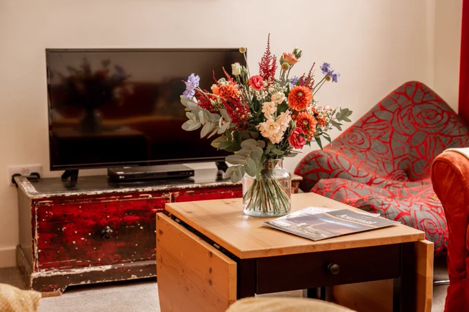 Vase of flowers on a coffee table, with a TV and chair in the background