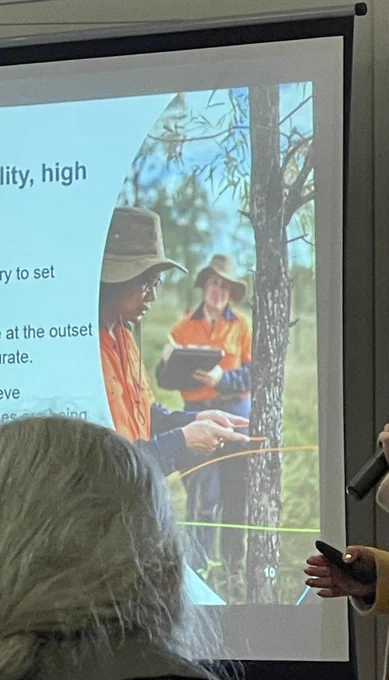 Photo of a photo of two people wearing hi-vis. One person is holding a clipboard. The other person is measuring a tree with a pair of calipers.