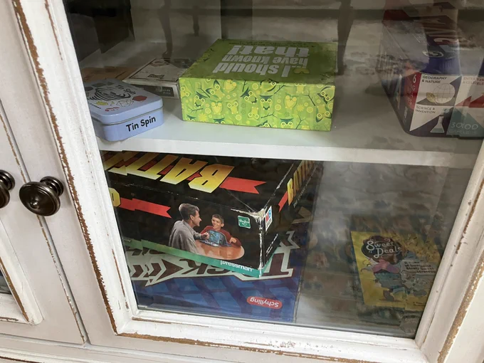 Cabinet showing battleship and a couple other board games including Tin Spin and Sweet Deals