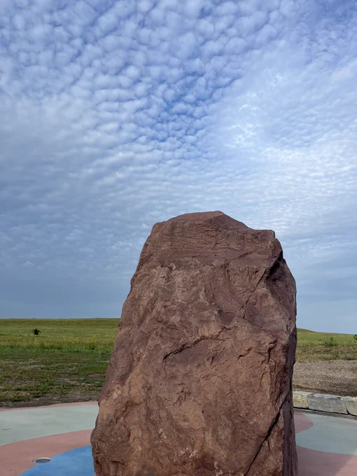 Red quartzite boulder backgrounded by green prairie and a blue sky.
