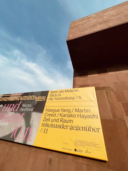 Ein Ausschnitt der Plakatwand an der Kunsthalle Bielefeld kündigt die aktuelle Ausgabe 11 der Ausstellungsreihe "miteinander gegenüber" an, in der sich Werke von Hague Yang, Martin Creed und Kanako Hayashi zum Thema "Zeit und Raum" begegnen.
Foto: Marina Böddeker
