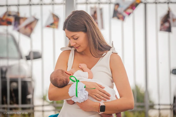A woman breastfeeds her baby while standing up.