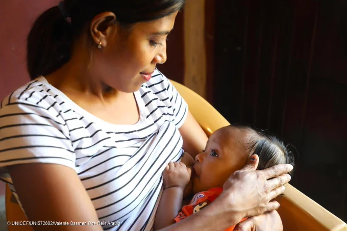 A woman breastfeeds her baby while sitting down on a chair.